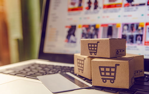 Laptop with credit card and mini boxes with trolley icons.